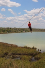 guest riding the zip line from the observation tower over the coba lagoon