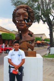 Most resort area's in Mexico have tourist police who offer a variety of services to visitors . Here is one of Comitan's finest, Senor Lopez, standing in front of a metal sculpture in the plaza.